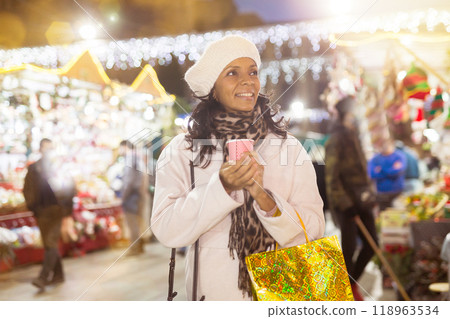 Happy latina with paper cup of coffee visiting city Christmas fair Happy latina with paper cup of coffee visiting city Christmas fair 118963534