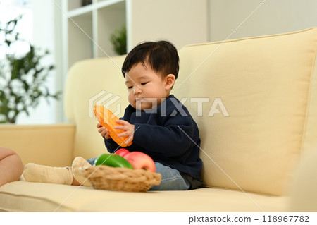 Little baby playing with vegetable toys on sofa at home. Child care concept Little baby playing with vegetable toys on sofa at home. Child care concept 118967782