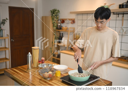 Young man stirring ingredients in a green pan with spatula. People, food and lifestyle concept 118967834