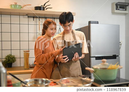 Loving young Asian couple cooking in the kitchen and looking at recipe on digital tablet Loving young Asian couple cooking in the kitchen and looking at recipe on digital tablet 118967839