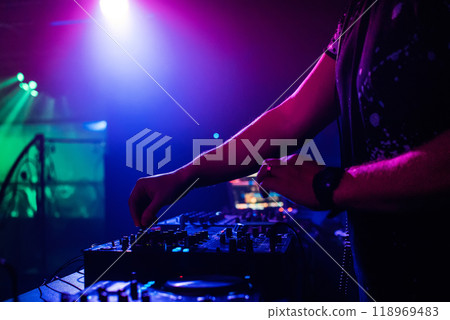 DJ in night club playing at professional mixer, color-changing spotlights 118969483