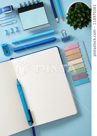 Top view of a neat desk. Open notebook with a blank page, blue office supplies pens, pencils, felt-tip pens, sharpener, stickers. Copyspace. Top view of a neat desk. Open notebook with a blank page, blue office supplies pens, pencils, felt-tip pens, sharpener, stickers. Copyspace. 118970361