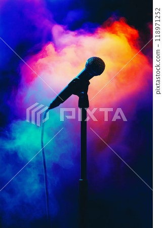 Microphone standing on an empty stage with colorful light and smoke. Mic on a stage Microphone standing on an empty stage with colorful light and smoke. Mic on a stage 118971252