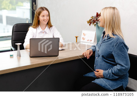 Young pregnant woman visiting her gynecologist in modern clinic. Woman sitting on chair and talking to her doctor 118973105