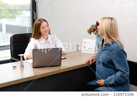 Young pregnant woman visiting her gynecologist in modern clinic. Woman sitting on chair and talking to her doctor 118973106