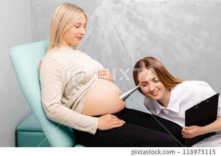 A gynecologist leans a stethoscope to a pregnant woman's belly and listens to the baby's heartbeat 118973115