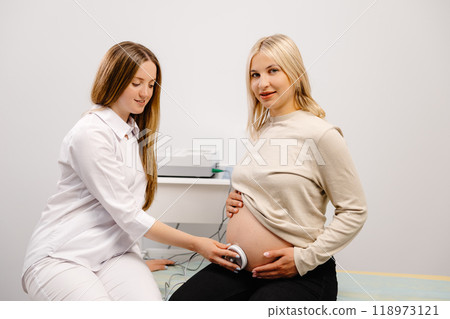 Doctor prepares a pregnant woman for checking fetal heartbeat by fetal monitoring. 118973121