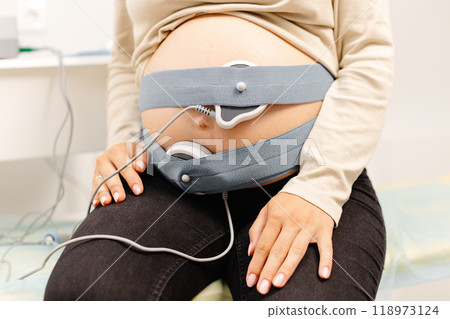 Woman pregnant checking fetal heart beat by fetal monitoring. Expectant mother with midwife adjusting sensors off cardiotocography Woman pregnant checking fetal heart beat by fetal monitoring. Expectant mother with midwife adjusting sensors off cardiotocography 118973124