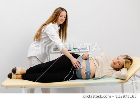 Doctor prepares a pregnant woman for checking fetal heartbeat by fetal monitoring. Doctor prepares a pregnant woman for checking fetal heartbeat by fetal monitoring. 118973163