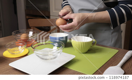 Process of making dough. Woman separates egg white from yolk in kitchen. Scales and eggs, utensils on wooden table. Baking macarons at home. Hands in close-up. Process of making dough. Woman separates egg white from yolk in kitchen. Scales and eggs, utensils on wooden table. Baking macarons at home. Hands in close-up. 118974187