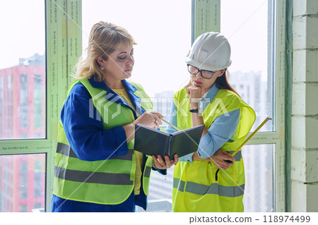 Two female industrial workers at construction site discussing work Two female industrial workers at construction site discussing work 118974499