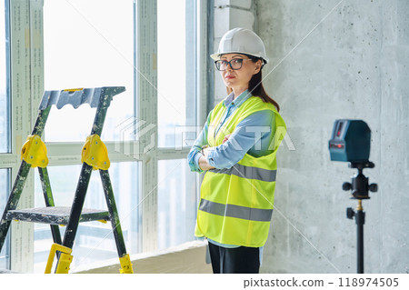 Woman in safety vest hard hat with crossed arms on new residential or commercial real estate site 118974505