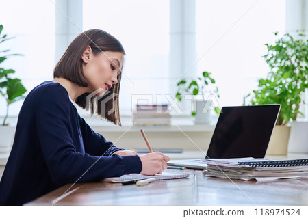 Young serious woman studying working writing in notebook, sitting at home at desk Young serious woman studying working writing in notebook, sitting at home at desk 118974524