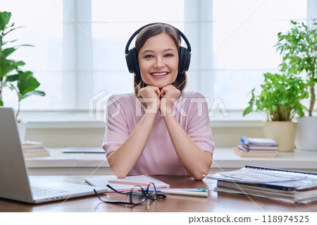Portrait of young female student wearing headphones, sitting at home at desk Portrait of young female student wearing headphones, sitting at home at desk 118974525