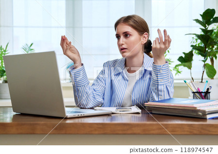 Teenage girl student studying online sitting at home at desk using laptop for video conference 118974547