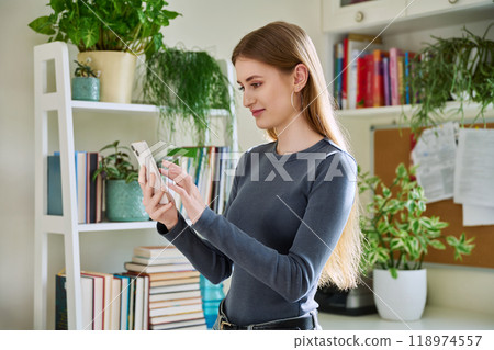 Happy female teenager using smartphone, standing at home 118974557