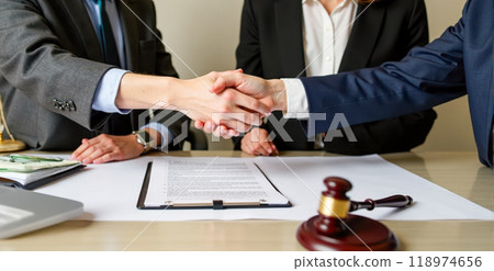 Handshake over legal documents with gavel and money on table symbolizing completed agreement in law office setting Handshake over legal documents with gavel and money on table symbolizing completed agreement in law office setting 118974656