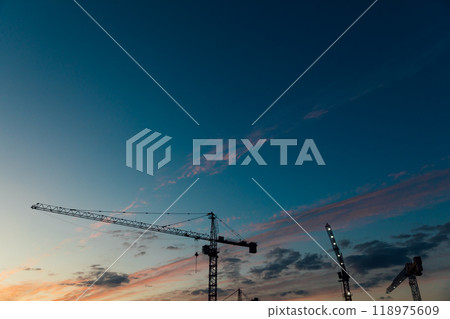 Construction cranes on the background of a sunset sky with clouds 118975609