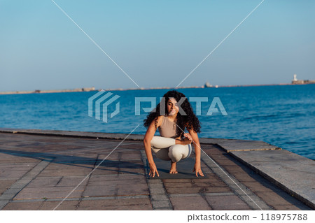 Athletic woman doing gymnastics yoga asana by the sea Athletic woman doing gymnastics yoga asana by the sea 118975788