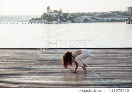 Pretty healthy woman doing active training exercise on a yoga mat near the ocean. Coastal yoga tranquility Pretty healthy woman doing active training exercise on a yoga mat near the ocean. Coastal yoga tranquility 118975790