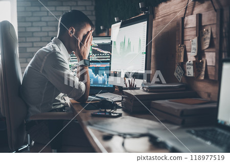 Stressful day at the office. Young businessman holding hands on his face while sitting at the desk in creative office Stressful day at the office. Young businessman holding hands on his face while sitting at the desk in creative office 118977519