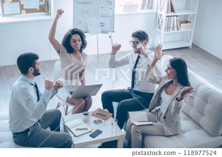 Successful team. Top view of group of four young people gesturing and looking happy while sitting on the couch at office 118977524