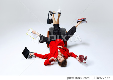Businesswoman balancing her tasks with one foot in air, holding clipboard, calculator, and coffee. Power dressing meets multitasking chaos. Businesswoman balancing her tasks with one foot in air, holding clipboard, calculator, and coffee. Power dressing meets multitasking chaos. 118977556