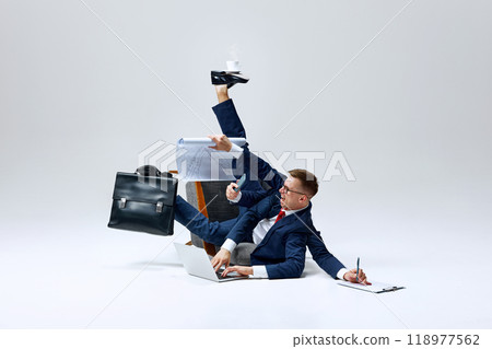 Businessman juggling multiple tasks, papers flying as he multitasks on floor. Overloaded but determined to stay on top of his workload. 118977562