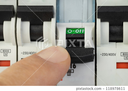 Hand turning off electrical circuit breaker in control panel 118978611