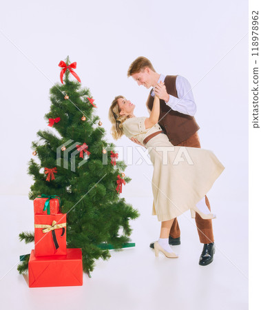 Couple shares romantic moment dancing beside Christmas tree, surrounded by holiday decorations and festive atmosphere. Couple shares romantic moment dancing beside Christmas tree, surrounded by holiday decorations and festive atmosphere. 118978962