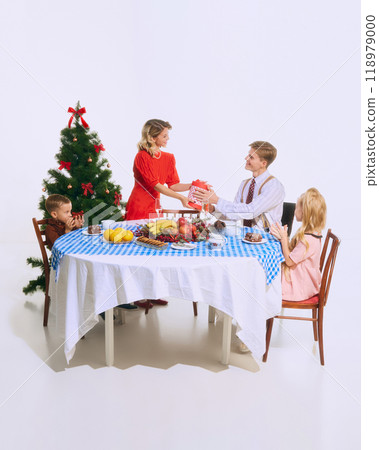 Family exchanges gifts at Christmas table. Excitement of giving and receiving adds magical touch to holiday atmosphere. 118979000