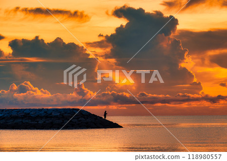 Fisherman standing and fishing on seashore with golden sky in tropical sea 118980557
