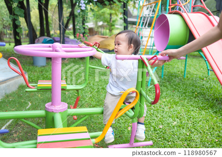 Asian toddler boy having fun with merry go round on the grass at playground Asian toddler boy having fun with merry go round on the grass at playground 118980567