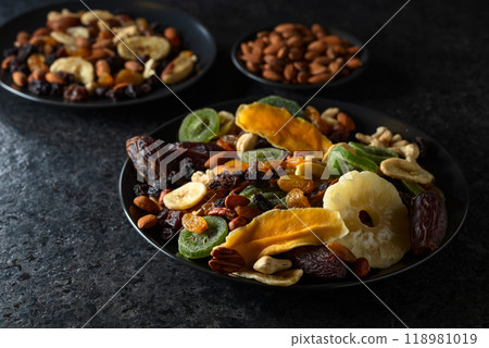 Dried tropical fruits, nuts, and raisins in black plate. 118981019