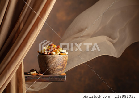 The mix of various nuts and raisins in a wooden bowl on a brown background. 118981033