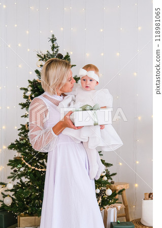 Mother and daughter holding a New Year's gift at the Christmas tree Mother and daughter holding a New Year's gift at the Christmas tree 118981065