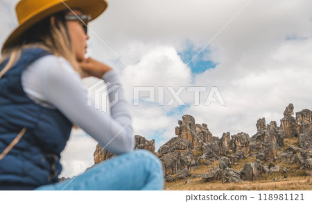 A woman wearing a yellow hat and blue jeans is sitting on a rock in a Huayllay Stone Forest, Peru. A woman wearing a yellow hat and blue jeans is sitting on a rock in a Huayllay Stone Forest, Peru. 118981121