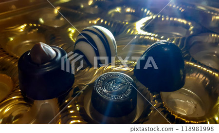Beautiful chocolate candies. Candies of different shapes in golden packaging, illuminated by a beam of light. 118981998