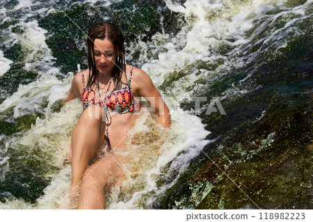 Beautiful girl enjoys swimming in a stream of a rapid mountain river at resort 118982223