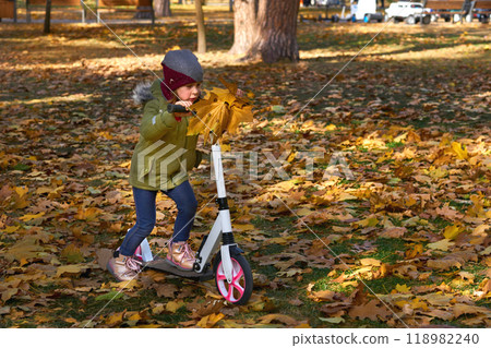 A small child on a push scooter carries a bouquet of autumn leaves to his mother 118982240