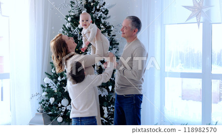 Joyous family comes together around a christmas tree, cherishing the festive season with their little one. Smiling, playing, and forming precious memories in their warm and loving home Joyous family comes together around a christmas tree, cherishing the festive season with their little one. Smiling, playing, and forming precious memories in their warm and loving home 118982570