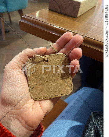 Close-up hand holds a small wooden tag with a twine loop. Copy space and empty place for text. Natural texture and simplicity of the tag create a connection to artisanal craftsmanship Close-up hand holds a small wooden tag with a twine loop. Copy space and empty place for text. Natural texture and simplicity of the tag create a connection to artisanal craftsmanship 118984163