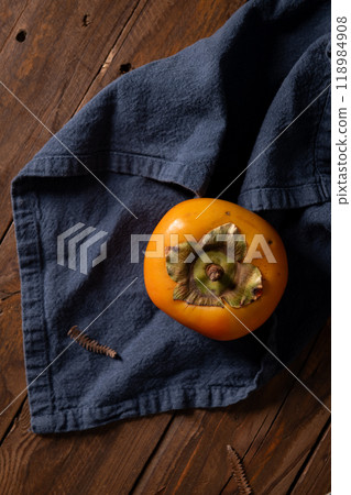 A single ripe persimmon rests on a dark wooden surface A single ripe persimmon rests on a dark wooden surface 118984908