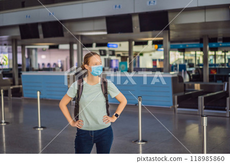 Woman in mask at empty airport at check in in coronavirus quarantine isolation, returning home, flight cancellation, pandemic infection worldwide spread, travel restrictions and border shutdown 118985860