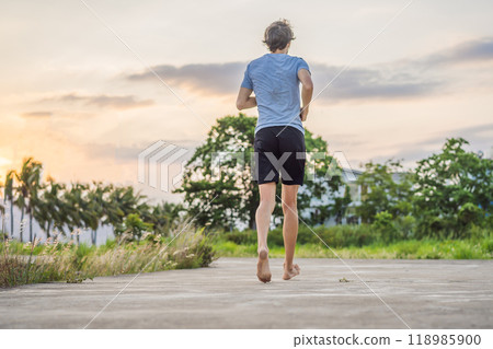 A man runner is engaged in jogging on a concrete path without shoes, without sneakers, for health A man runner is engaged in jogging on a concrete path without shoes, without sneakers, for health 118985900