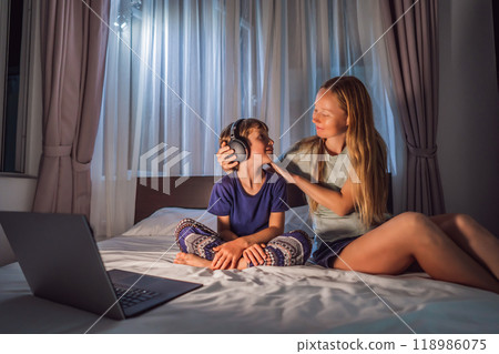 Mom helps her son to put on headphones. Boy meditates on bed using meditation app. sport, technology and healthy lifestyle concept 118986075