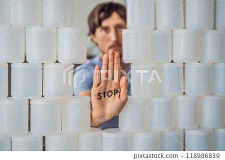 Man showing stop surrounded by many jars of yoghurt that he uses in a year. A huge amount of plastic food jars. Excessive consumption of plastic. Reduce, reuse, recycle 118986839