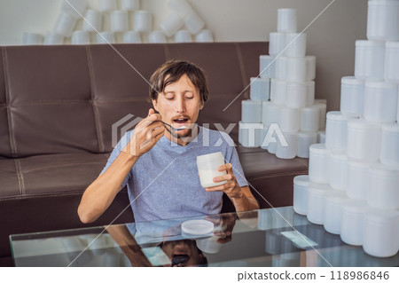 The man eats yogurt and is surrounded by many jars of yoghurt that he uses in a year. A huge amount of plastic food jars. Excessive consumption of plastic. Reduce, reuse, recycle The man eats yogurt and is surrounded by many jars of yoghurt that he uses in a year. A huge amount of plastic food jars. Excessive consumption of plastic. Reduce, reuse, recycle 118986846