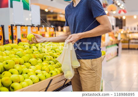 Man chooses apples in a supermarket without using a plastic bag. Reusable bag for buying vegetables. Zero waste concept Man chooses apples in a supermarket without using a plastic bag. Reusable bag for buying vegetables. Zero waste concept 118986895