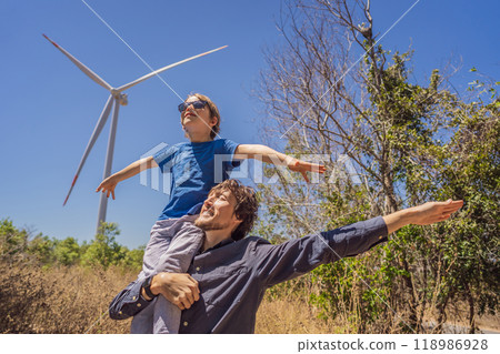 Alternative energy, wind farm and happy time with your family. Happy father carrying his son on shoulders is on vacation and escape to nature. Father carrying son on shoulders and waving their arms 118986928